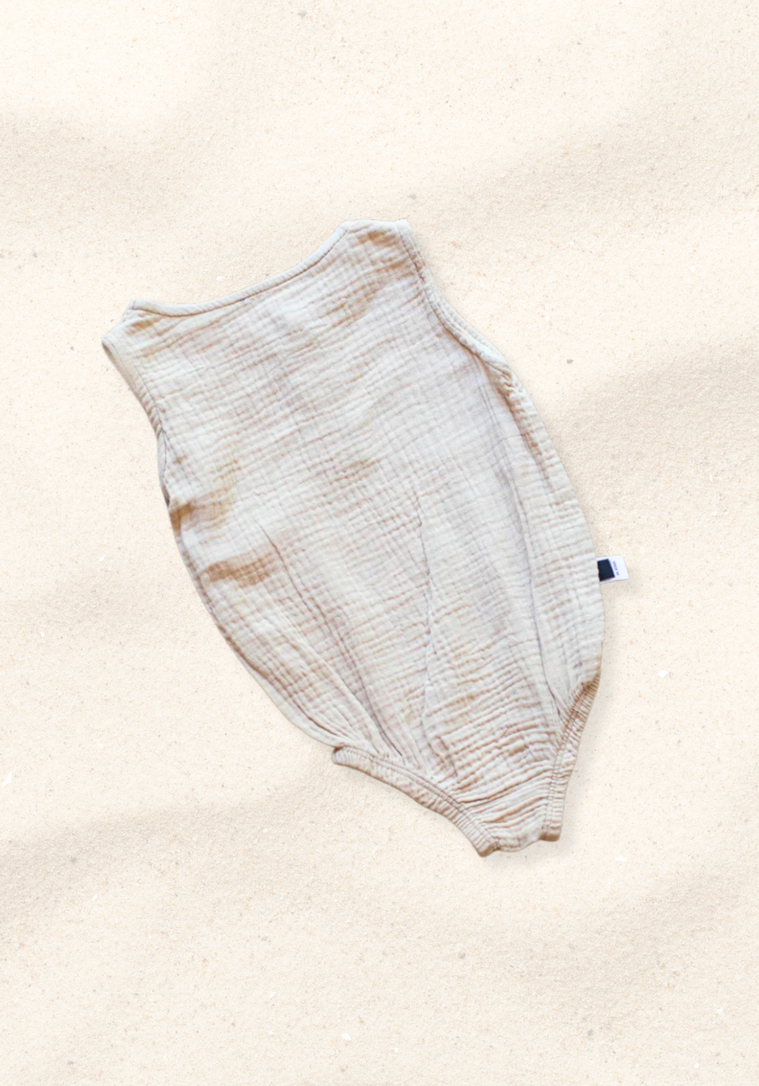 Beige baby romper made of organic cotton with wooden button front and soft texture, displayed on a sand background