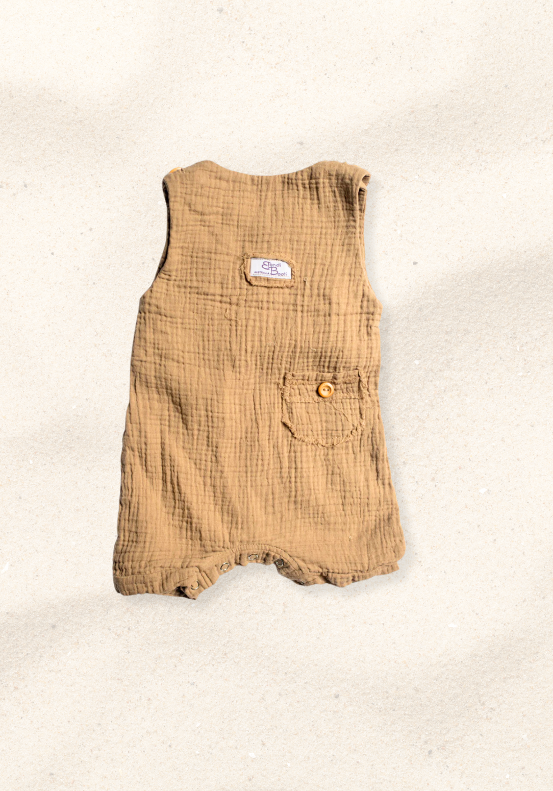 Mocha brown baby overall onesie made from organic cotton with adjustable straps and front pocket, laid flat on a sand-colored background