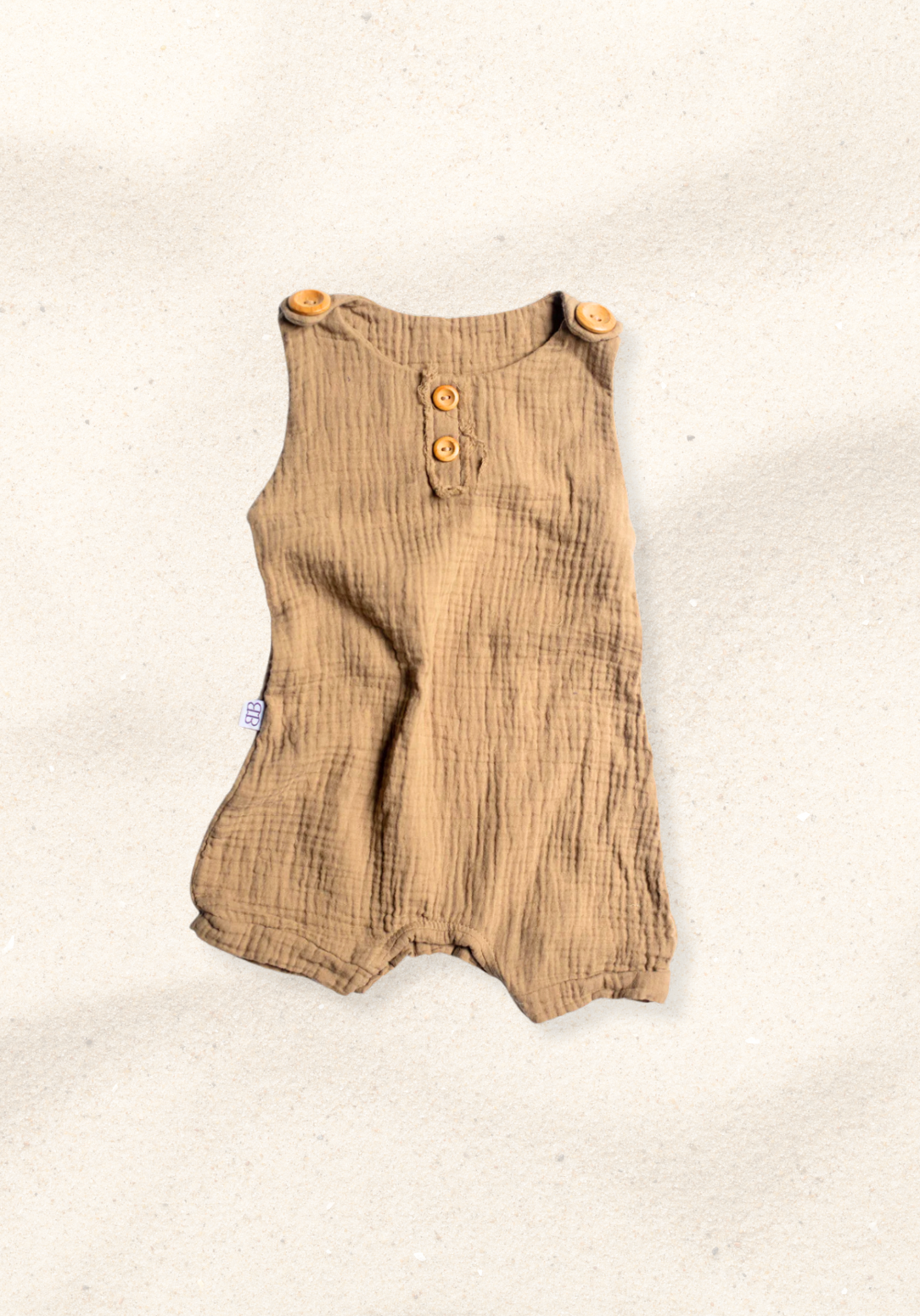 Mocha brown baby overall onesie made from organic cotton with adjustable straps and front pocket, laid flat on a sand-colored background