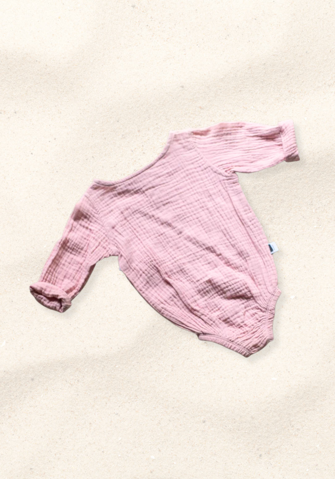 Back view of pink muslin baby romper with long sleeves and soft elastic hem on sand background