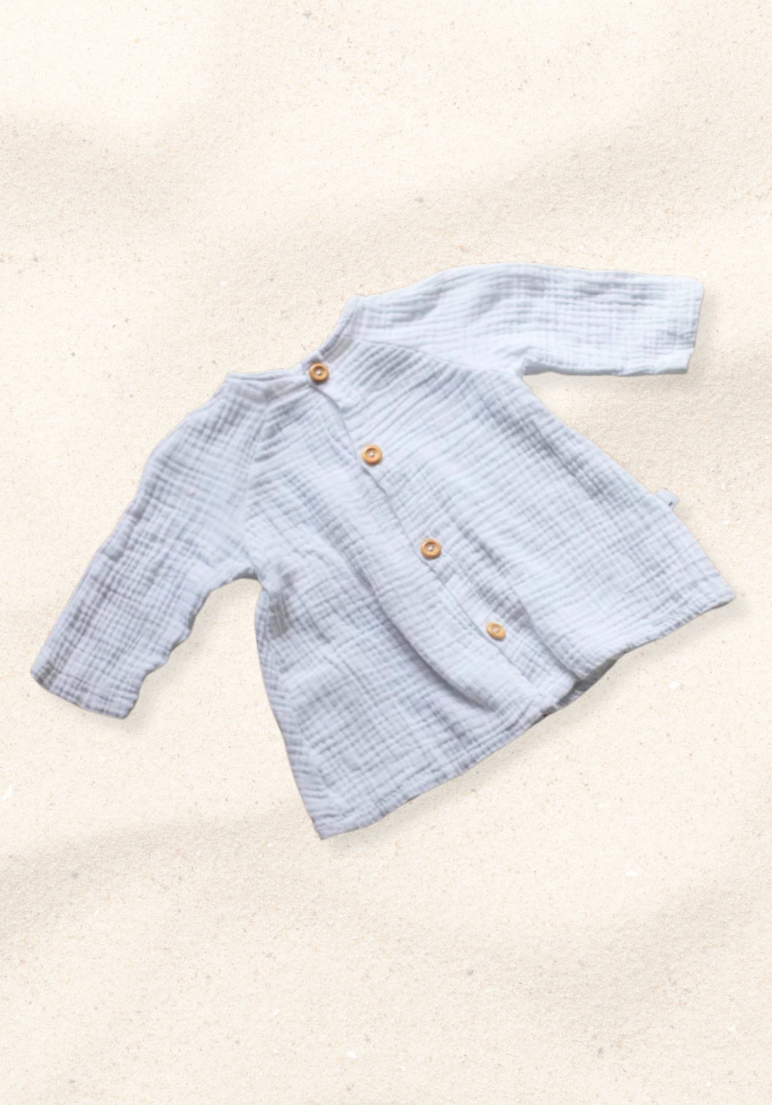 White boho-style baby dress with lace details laid flat on a sand-colored background, perfect for summer