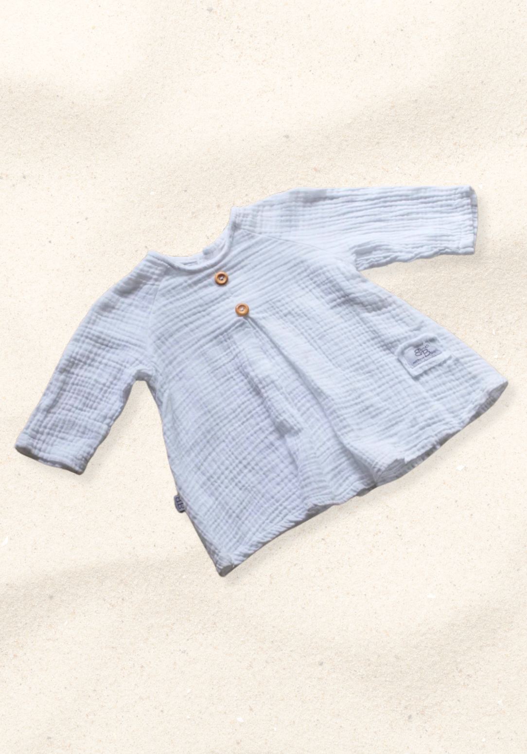 White boho-style baby dress with lace details laid flat on a sand-colored background, perfect for summer