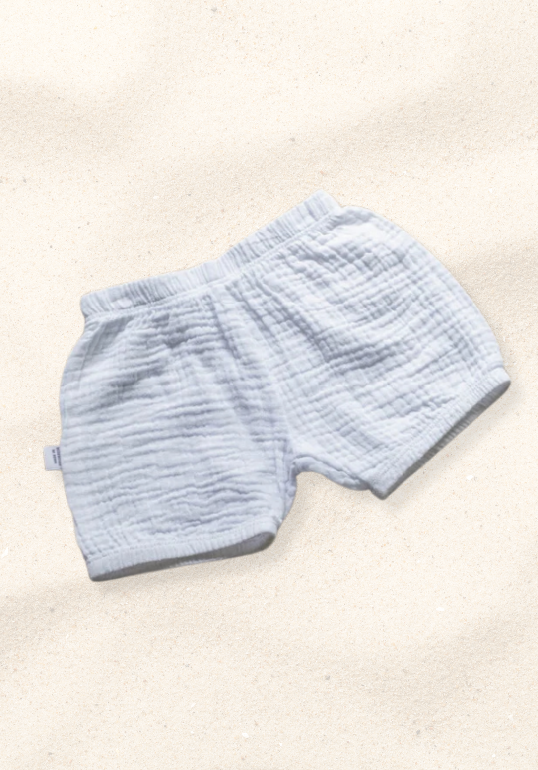 White organic cotton baby bloomers with soft elastic waist and leg openings, laid flat on a sand-colored background