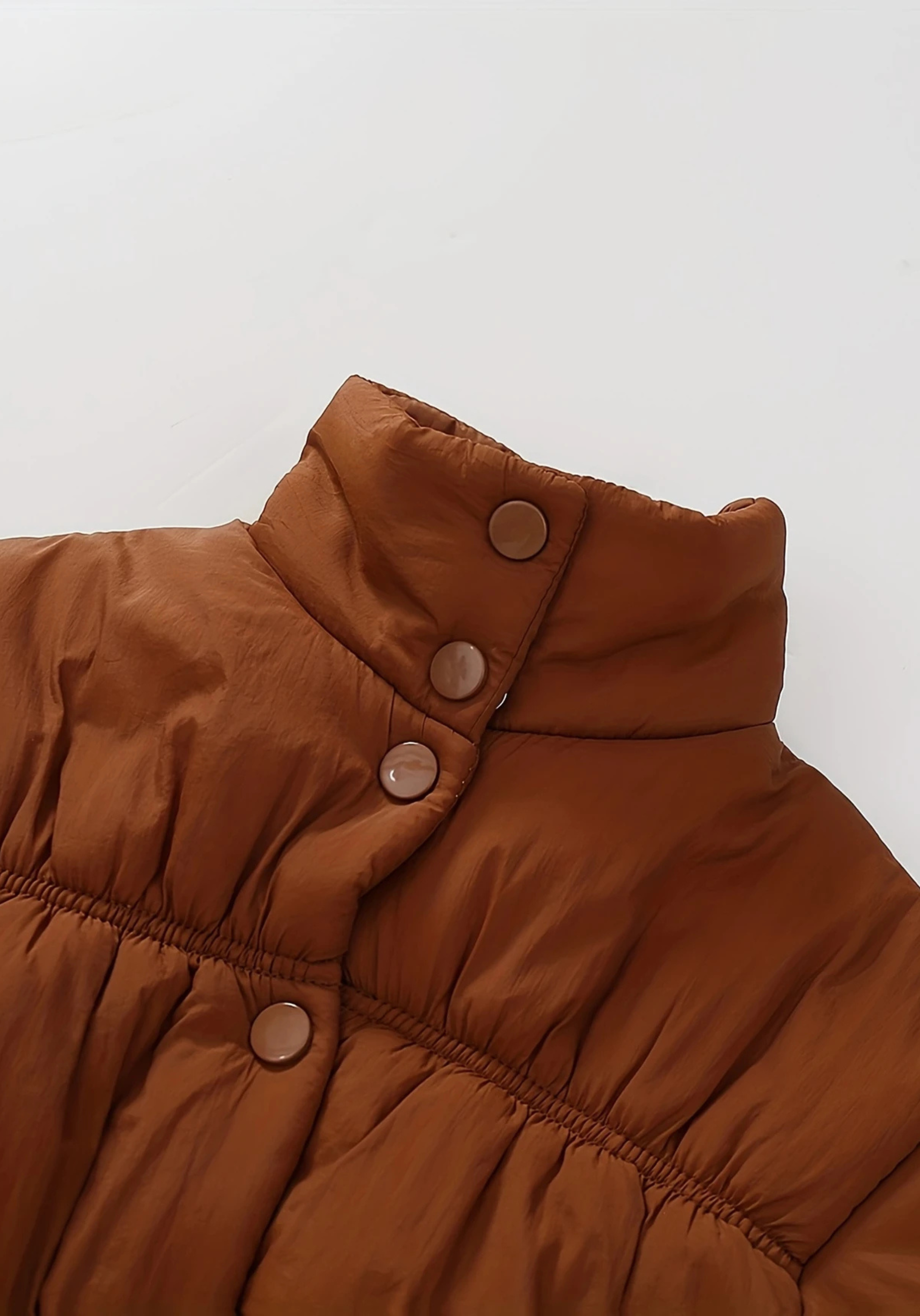 Close up view of toddler brown puffer jacket with ruched detailing and high collar