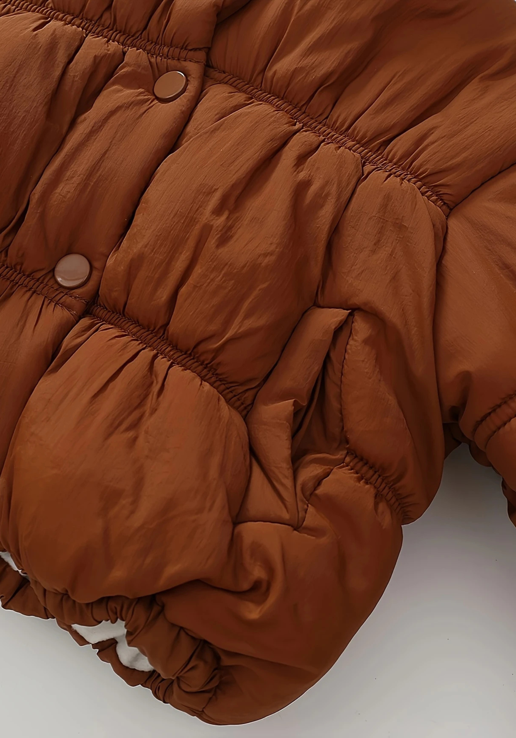 Close up view of toddler brown puffer jacket with ruched detailing and high collar