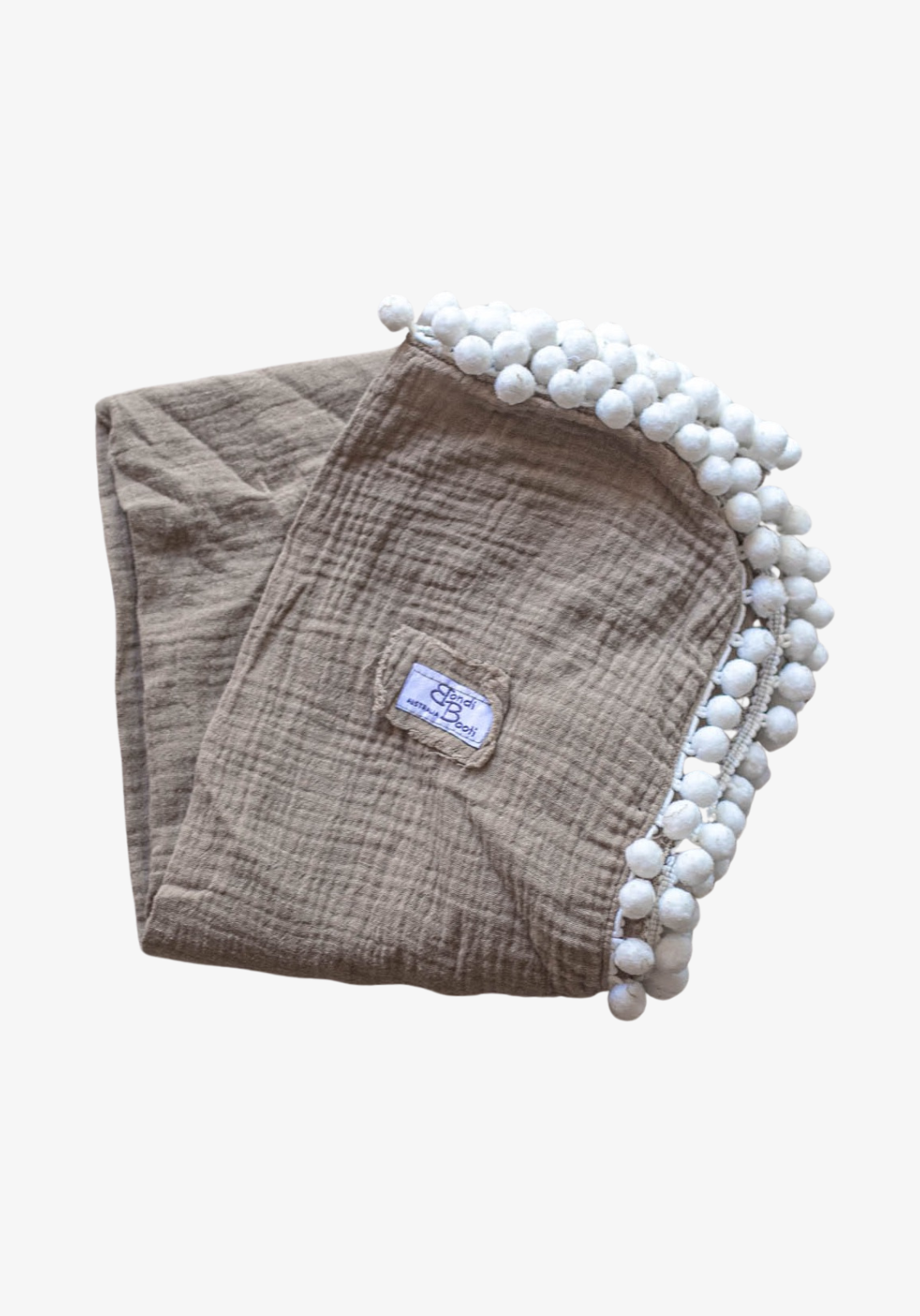 Taupe organic cotton baby blanket with white pom-pom trim, neatly folded with visible Bondi Booti label, displayed on a neutral background.