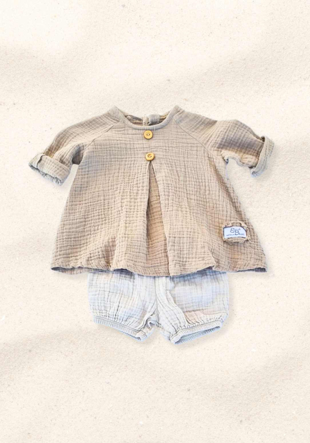 Mocha-colored cotton boho baby dress with embroidered hem, displayed on a sand background for a neutral look