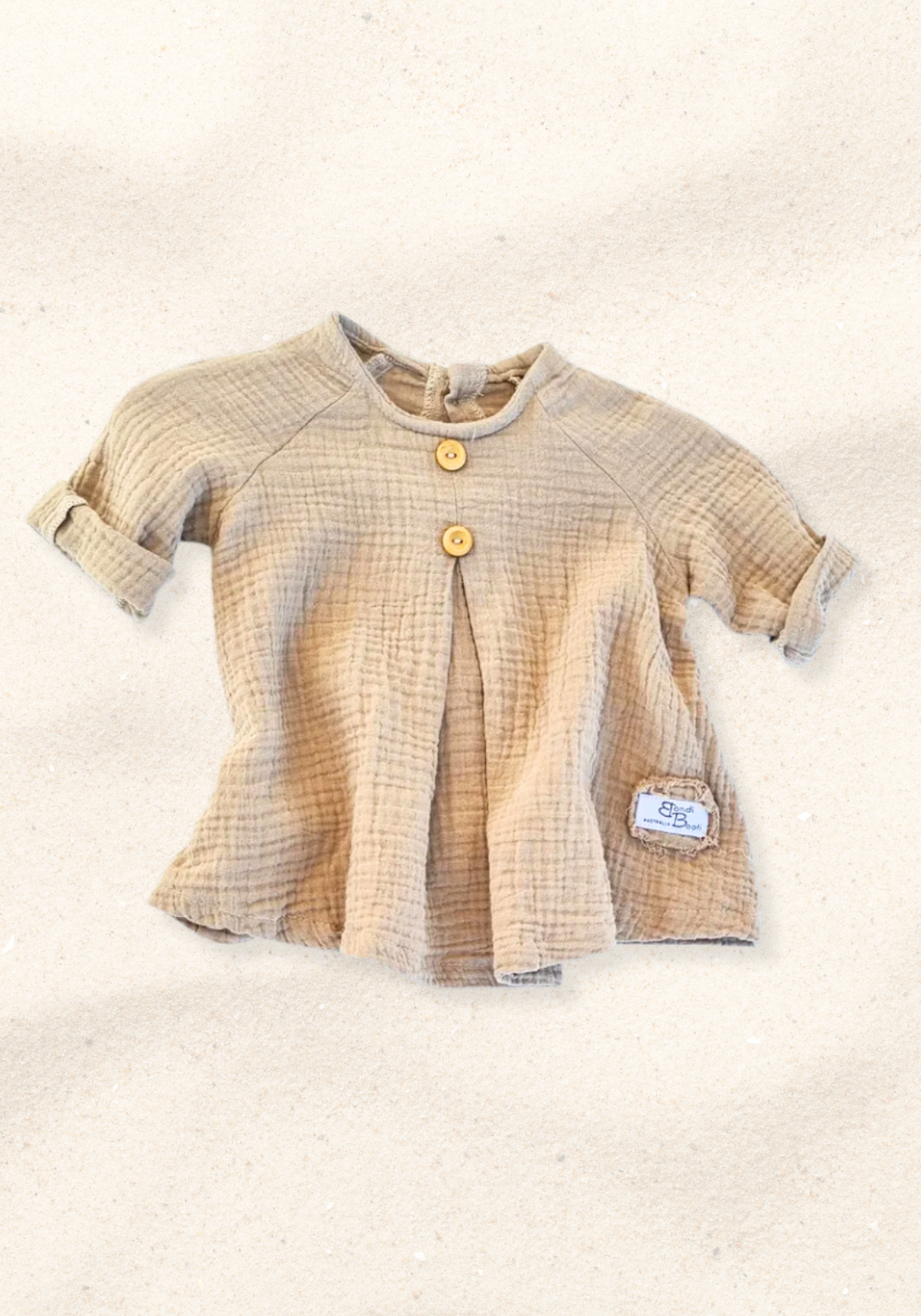 Mocha-colored cotton boho baby dress with embroidered hem, displayed on a sand background for a neutral look