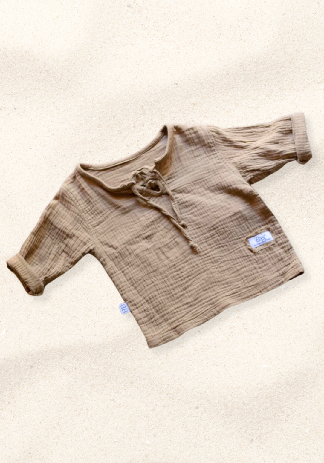 Mocha-colored pirate-style baby shirt with wooden buttons and long sleeves, laid flat on a sand-colored background